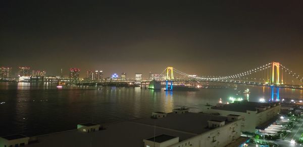 Illuminated bridge over river in city against sky at night