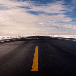 Empty road amidst field against cloudy sky during winter