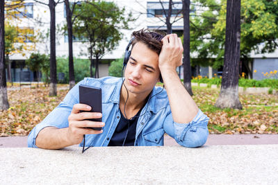 Man listening music while using mobile phone in city