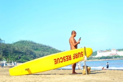 Man with yellow surfboard at beach against clear blue sky