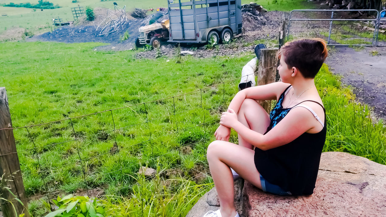 FULL LENGTH OF WOMAN SITTING ON GRASS AGAINST BUILDING