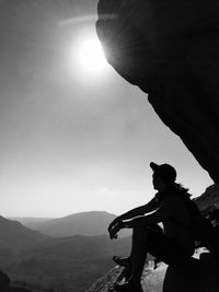 Full length of hiker sitting on cliff against clear sky