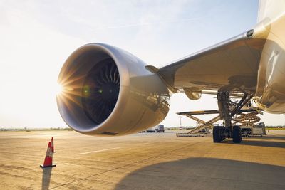 Busy airport at sunset. large jet engine against loading of cargo containers to airplane.