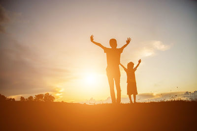 Silhouette friends standing on field against sky during sunset