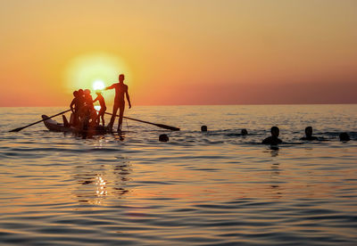 Silhouette people in sea against sky during sunset