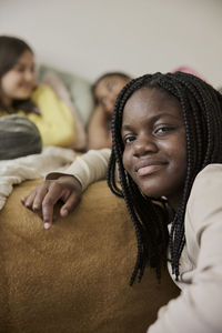Smiling teenage girl with braided hair by female friends lying in bedroom