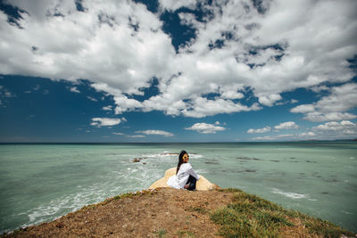 Woman sitting at beach against sky