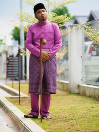 Full length of young man standing against pink wall