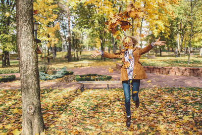 Full length of woman playing with leaves at park during autumn