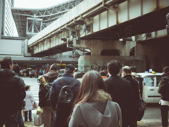 Rear view of people walking on city street by bridge