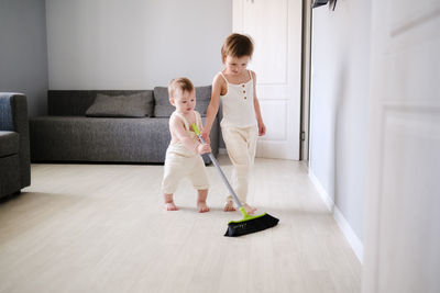 Children siblings with mop sweep floor in bright living room, help with housework and sibling 