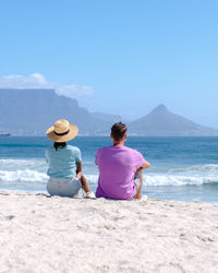 Rear view of woman sitting at beach against sky