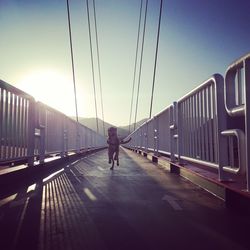 Rear view of man walking on railway bridge against sky