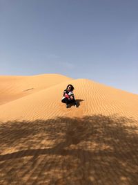 Low angle view of woman sitting on sand dune at desert against blue sky