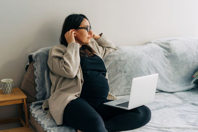Pregnant woman sitting at home on the couch working on the computer. person