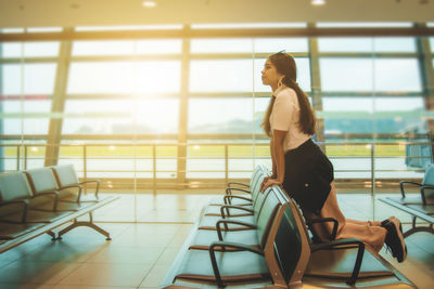 Side view of young woman standing against window