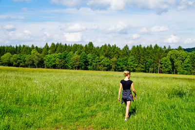 Rear view of woman walking on grassy field against sky