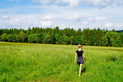 Full length of young woman standing on field against sky