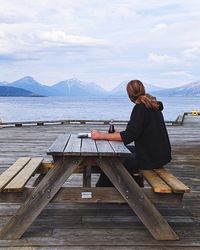 Man sitting on picnic table at pier in sea against sky