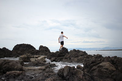 Man standing on rock formation by sea against sky