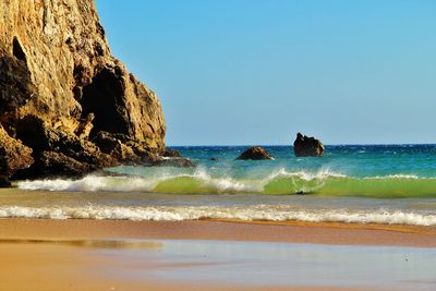 Scenic view of sea and waves against red rock and clear sky