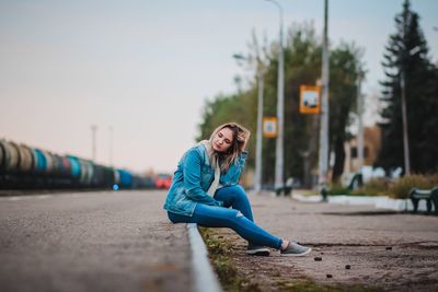 Portrait of young woman sitting in city against sky