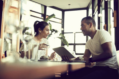 Low angle view of male and female with digital tablet talking while sitting at table in cafe