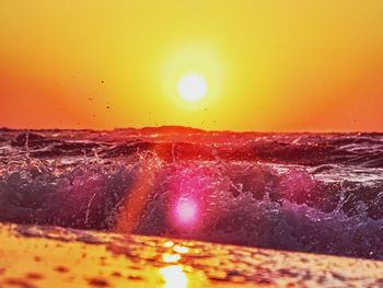 Close-up of sea waves splashing against orange sky