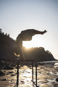 Shirtless young man practicing handstand on parallel bars at beach during sunset