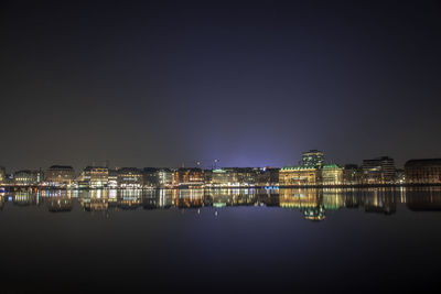 Illuminated buildings by river against sky at night