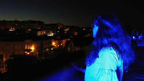 Woman standing by illuminated buildings in city at night