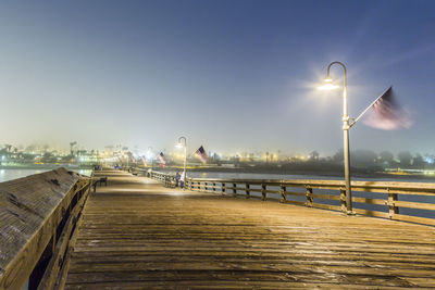 Street lights on pier by sea against sky