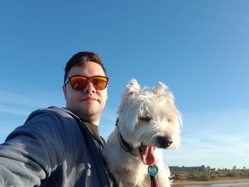 Low angle view of man wearing sunglasses with dog against sky
