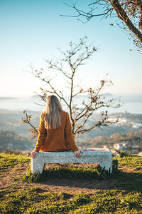 Rear view of woman sitting on land against sky
