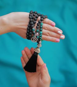 Close-up of cropped hand with bead necklace against blue background