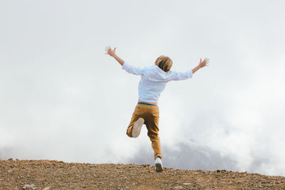 Rear view of boy jumping against sky