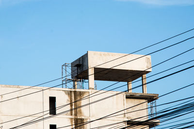 Low angle view of telephone pole against building against clear blue sky