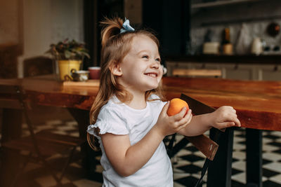 Funny little girl child in pajamas holding and eating an apple and laughing in the kitchen at home