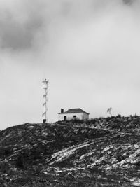 Lighthouse on field by building against sky