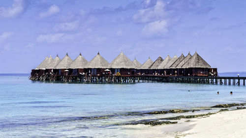 Stilt house on beach by sea against sky