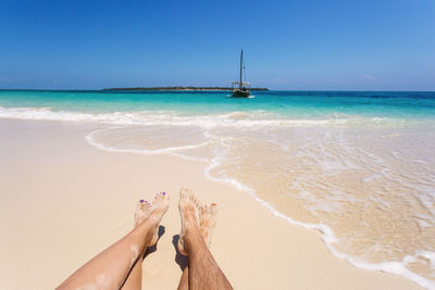 Low section of couple relaxing on beach against sky