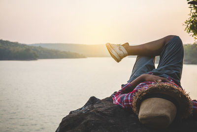 Midsection of woman sitting on rock against sky during sunset