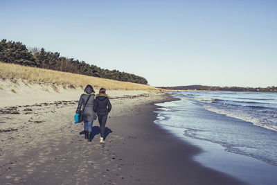 Rear view of people walking on beach against clear sky