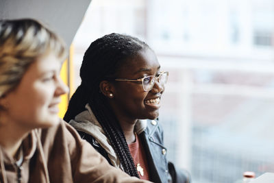 Happy teenage girl with braided hair wearing eyeglasses by female friend