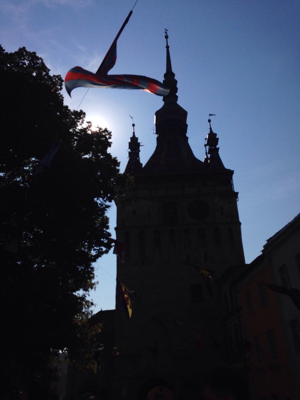 low angle view, building exterior, architecture, built structure, tree, religion, sky, place of worship, clear sky, spirituality, flag, tower, no people, outdoors, blue, church, tall - high, steeple, day