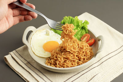 Cropped hand of person holding food in plate on table