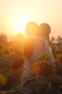 Rear view of girl with flowers against sky during sunset