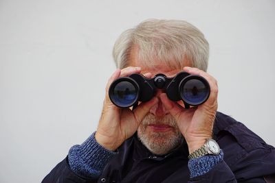 Close-up portrait of man looking through binoculars against gray background