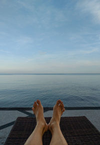 Low section of woman relaxing on beach against sky