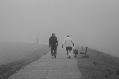 Rear view of men walking on road against sky